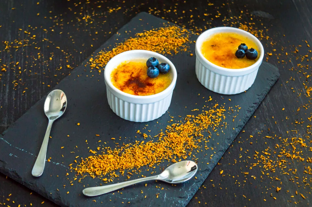 Small ramekin with vegan crème brûlée topped with a golden caramelized sugar crust and a vanilla pod beside it