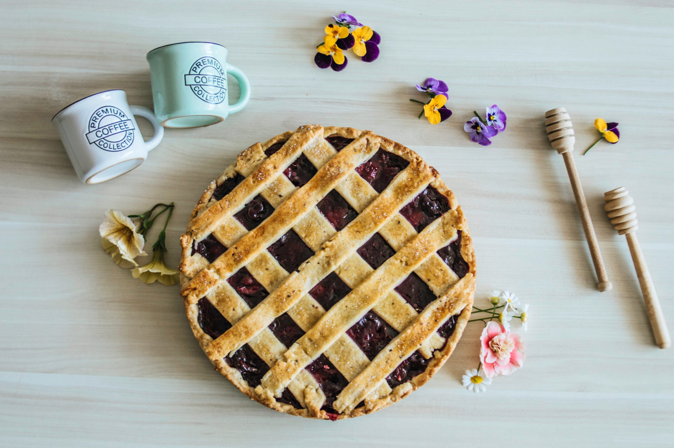 Homemade vegan cherry pie with golden lattice crust, decorated with edible flowers on a light wooden background