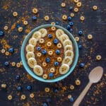 A warm bowl of chocolate semolina topped with fresh berries, banana slices, and a drizzle of peanut butter
