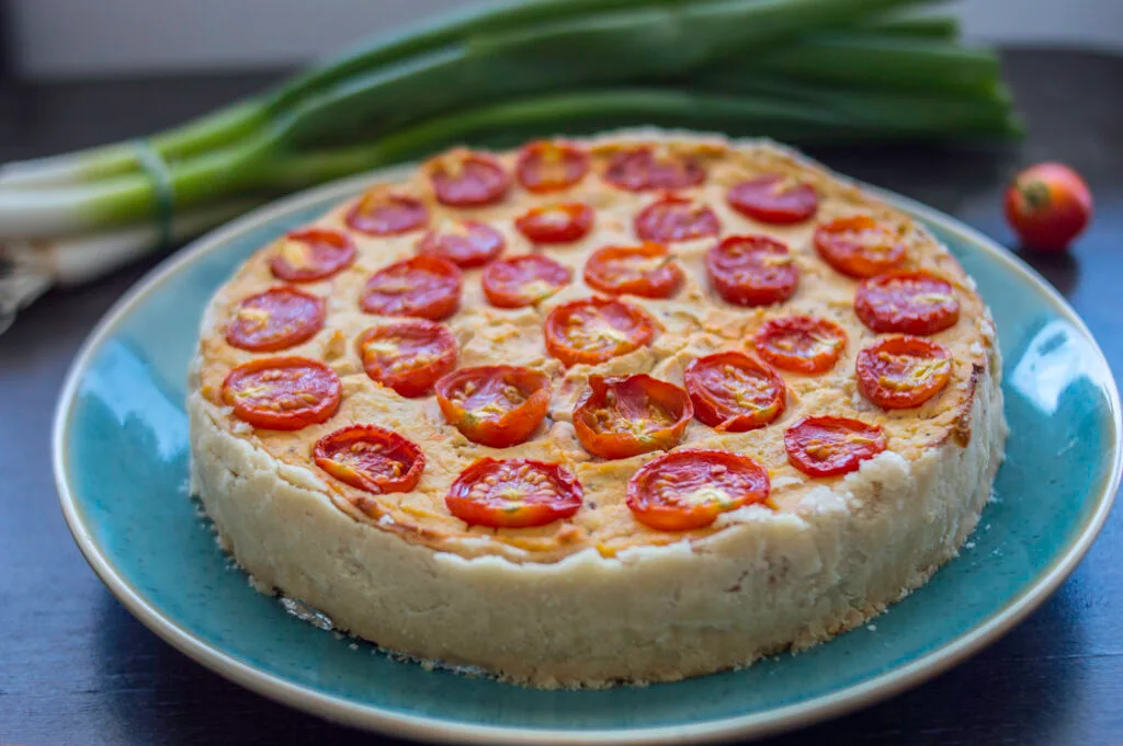 A golden baked vegan quiche with cherry tomato halves on top, served in a ceramic dish