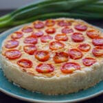 A golden baked vegan quiche with cherry tomato halves on top, served in a ceramic dish