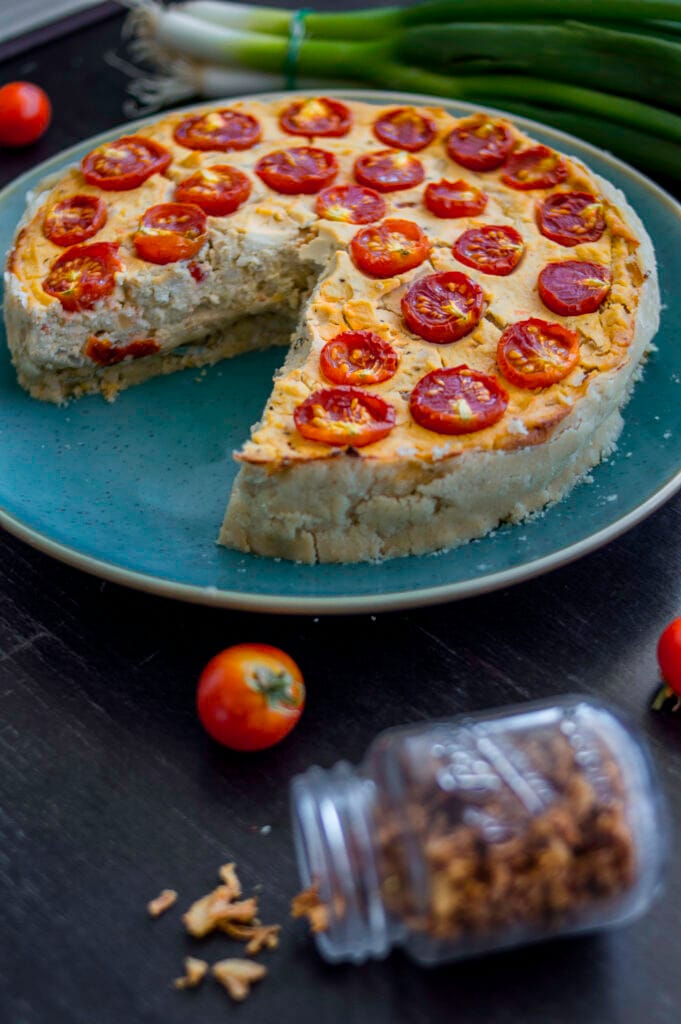 A golden baked vegan quiche with cherry tomato halves on top, served in a ceramic dish