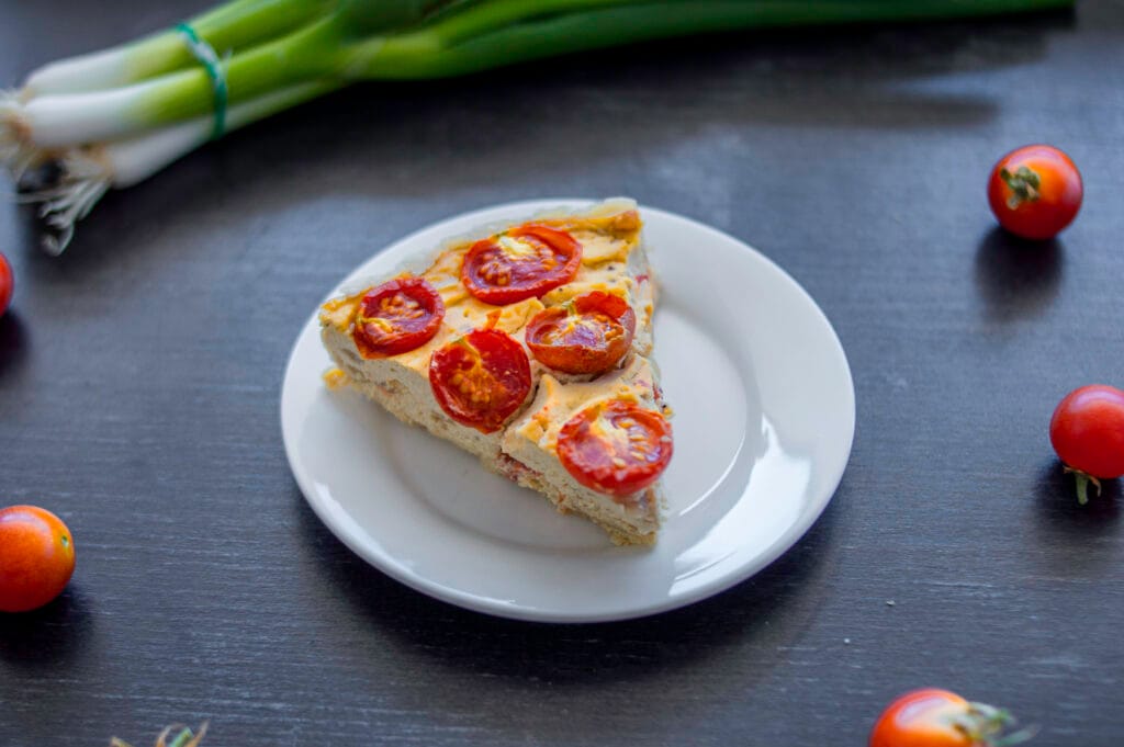 A golden baked vegan onion-tomato quiche with cherry tomato halves on top, served in a ceramic dish