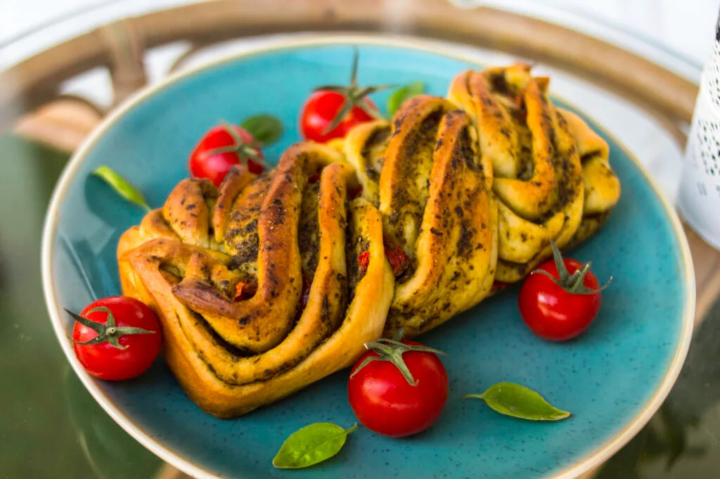 Close-up of sliced savory vegan tomato-pesto loaf with braided layers and golden crust
