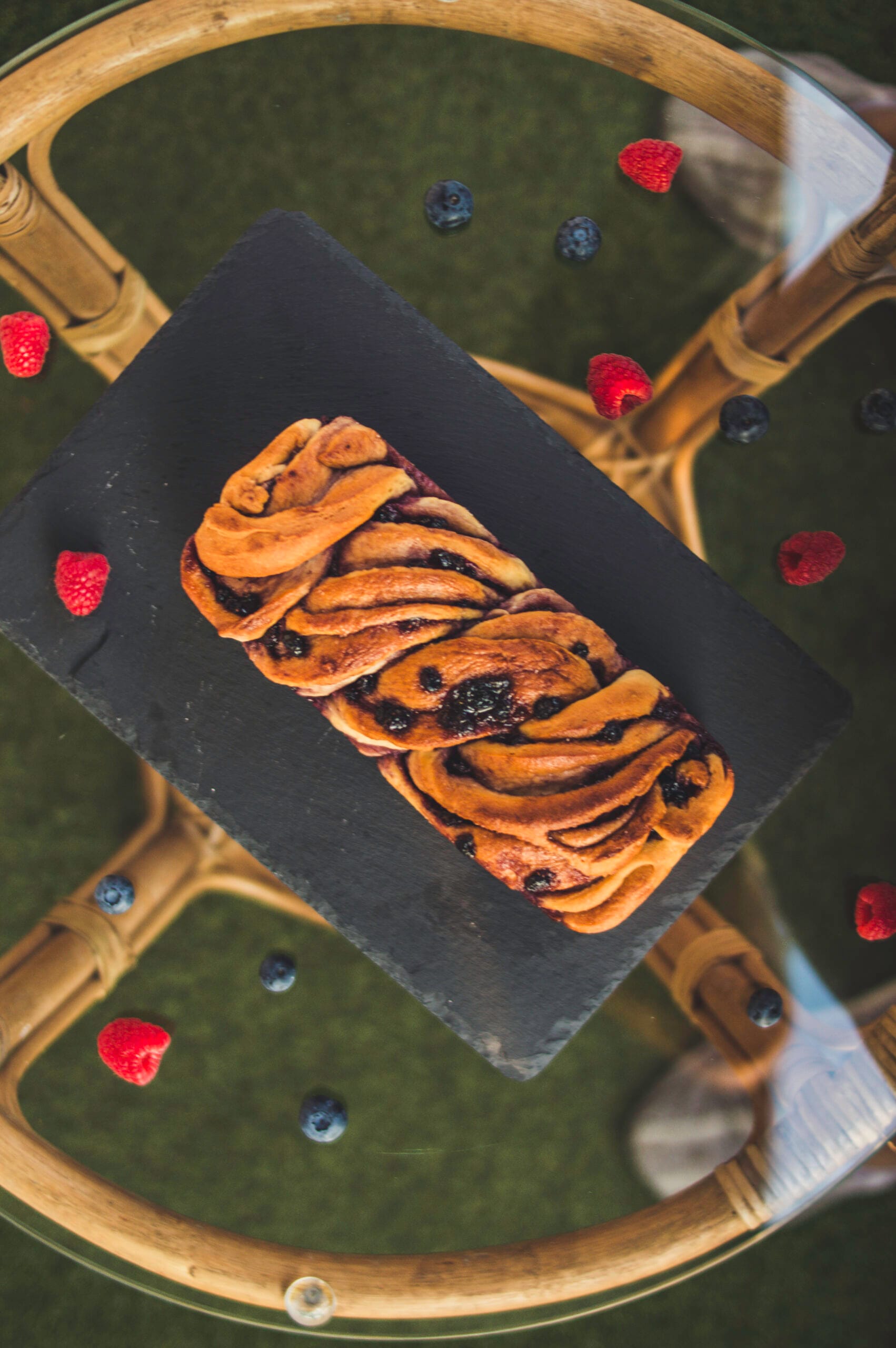 Sliced vegan babka with swirls of berry jam on a wooden board with crumbs and berries around