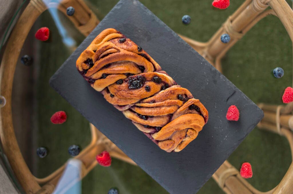 Sliced vegan babka with swirls of berry jam on a wooden board with crumbs and berries around