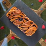 Sliced vegan babka with swirls of berry jam on a wooden board with crumbs and berries around