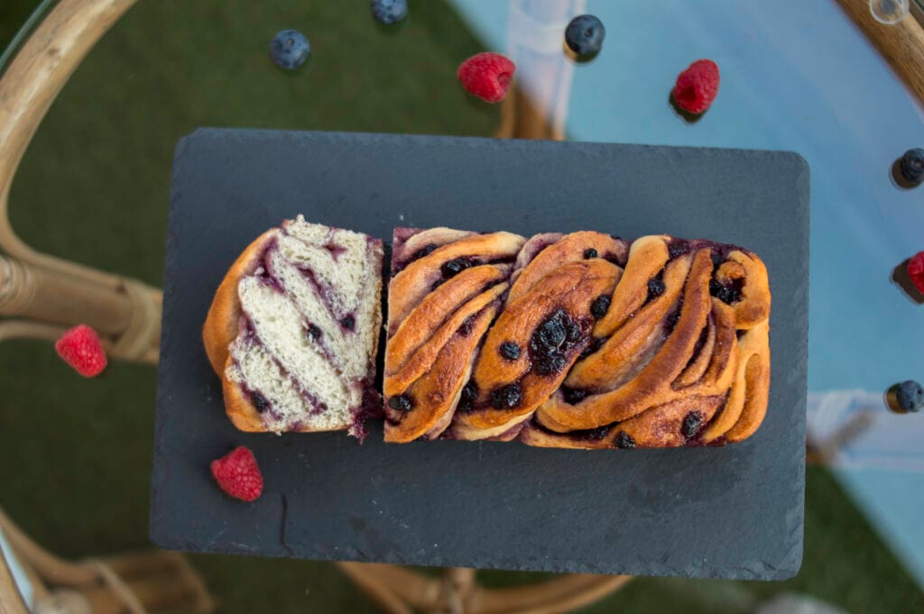 Sliced vegan babka with swirls of berry jam on a wooden board with crumbs and berries around