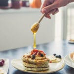 Stack of fluffy lemon poppy seed pancakes served with lemon slices and maple syrup on a white plate