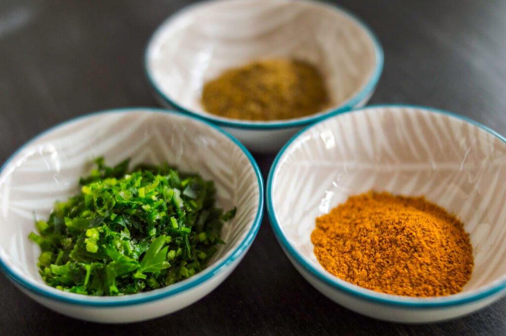 Small glass bowl of garam masala spice blend on a white kitchen counter with whole spices scattered nearby.