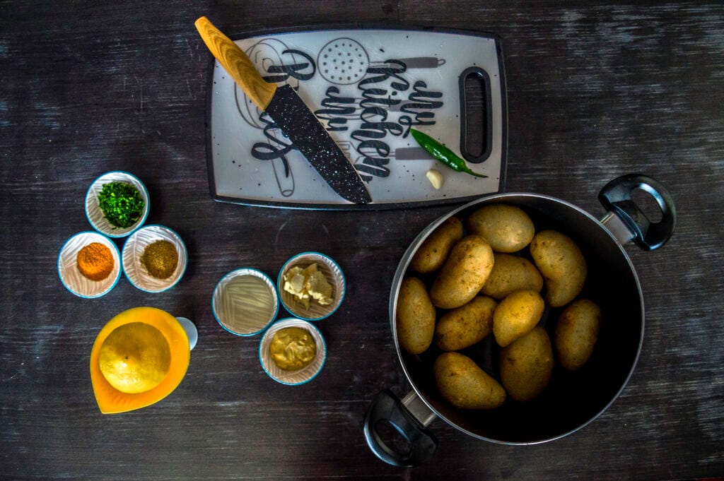 Flat lay of boiled potatoes and Indian spices on a dark countertop, ready to prepare Bombay potatoes.