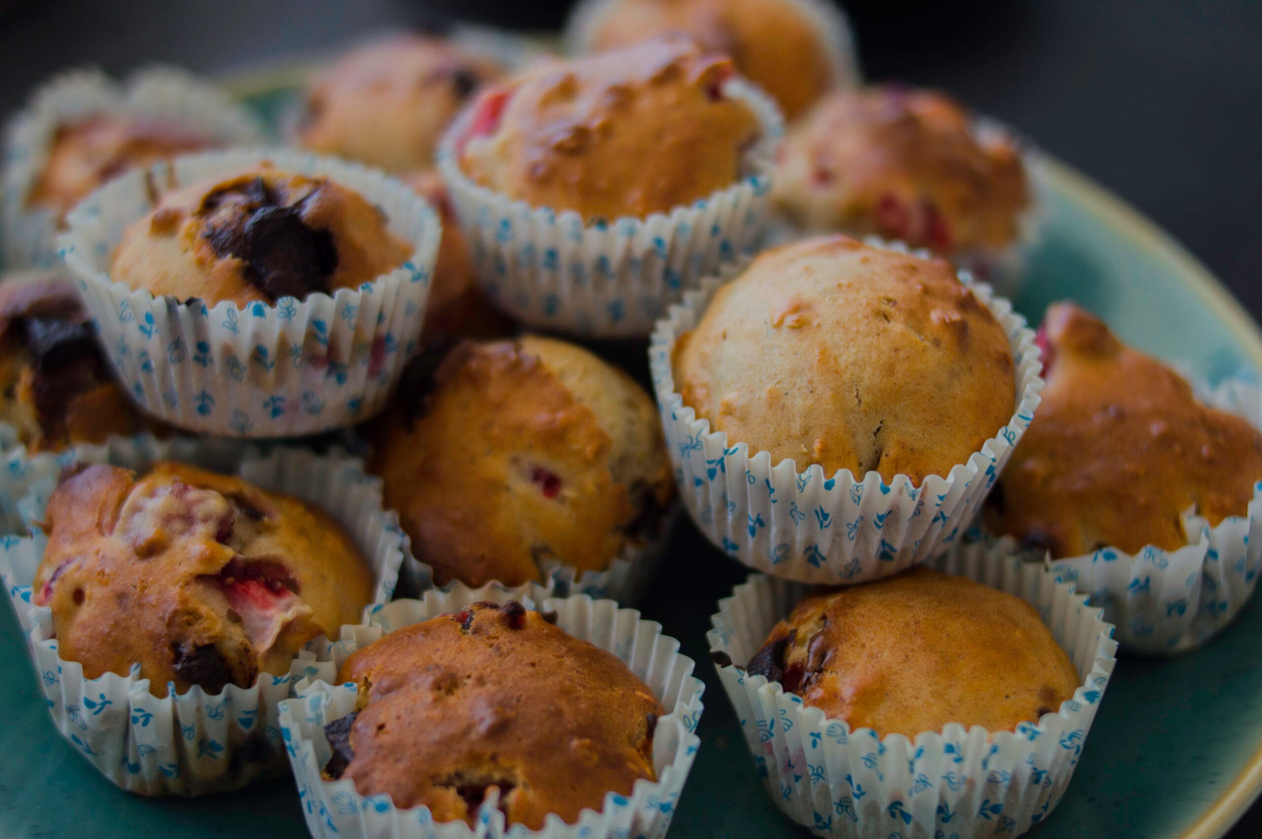 A batch of golden strawberry-banana muffins with melted chocolate chips on top.